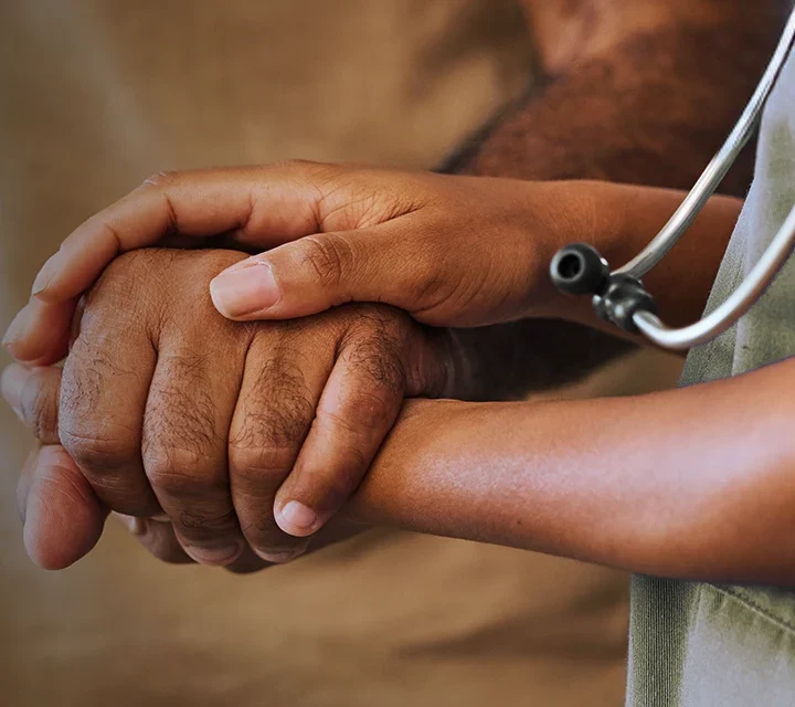 A nurse or doctor compassionately holding the hand of a patient