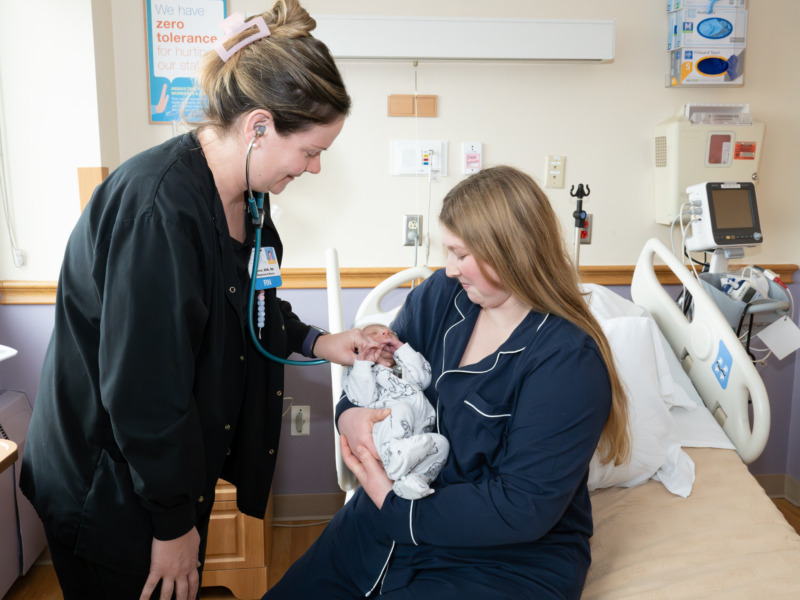 A nurse using a stethoscope to examine a newborn.